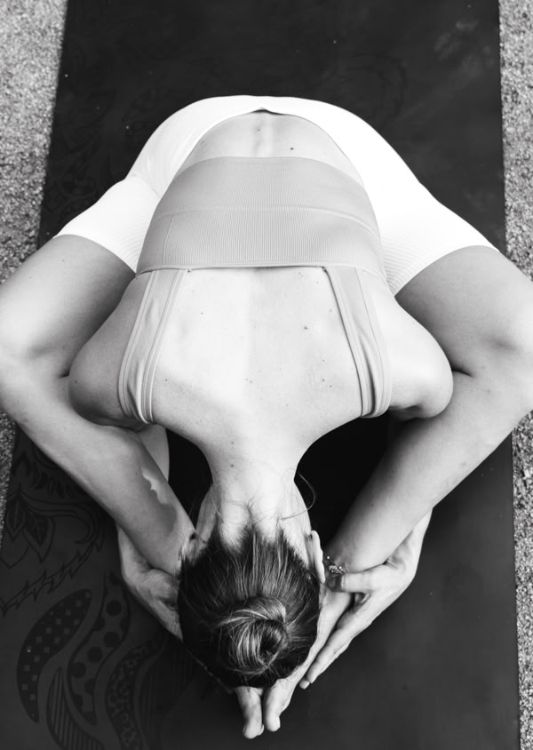 Person in einer Yoga-Pose auf einer Matte, von oben fotografiert, mit zusammengebundenem Haar und Sportkleidung.