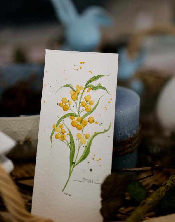 Karte mit gelben Blumenillustrationen, umgeben von blauen Kerzen und Dekorationen.