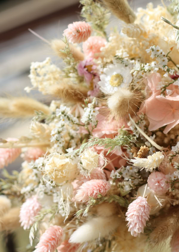 Ein Strauß aus getrockneten Blumen in Pastellfarben, darunter Rosa und Beige, liegt auf einem Geländer.