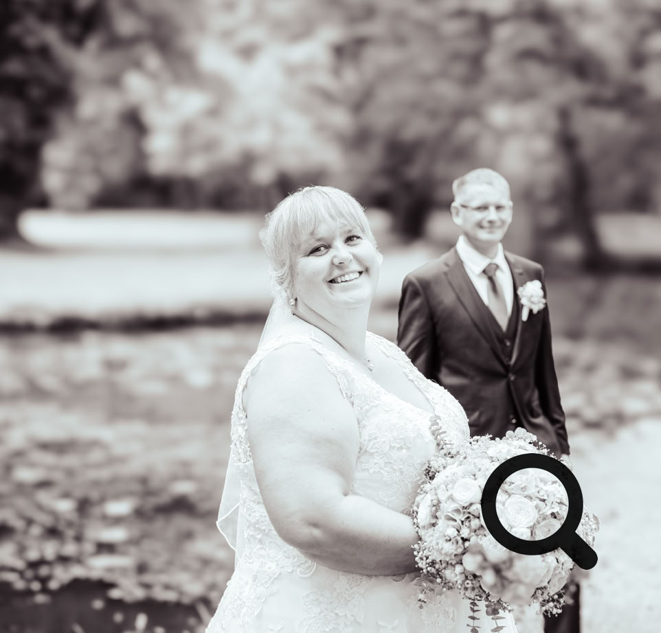 Ein Paar in farbenprächtigen traditionellen Hochzeitsgewändern sitzt inmitten kunstvoller Blumendekorationen.